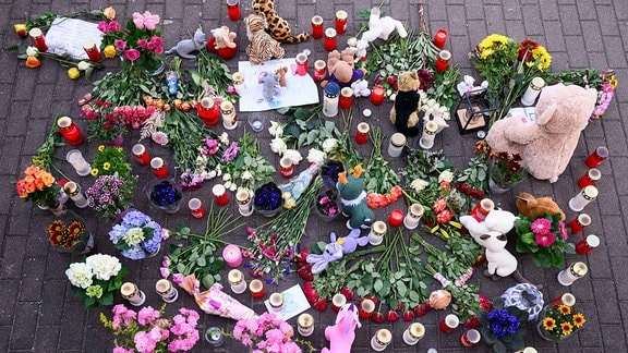 Blumen, Kerzen und Teddybären sind auf einem Fußweg abgelegt