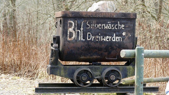 Ein mit Steinen gefüllter Bergbauförderkorb mit der Aufschrift Bahnhof Silberwäsche Dreiwerden.