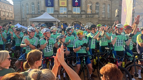 Eine Gruppe Radfahrer steht vor der Oper Chemnitz. Im Vordergrund jubelnde Menschen.