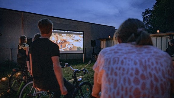 Menschen sehen in der Dämmerung auf eine Leinwand.