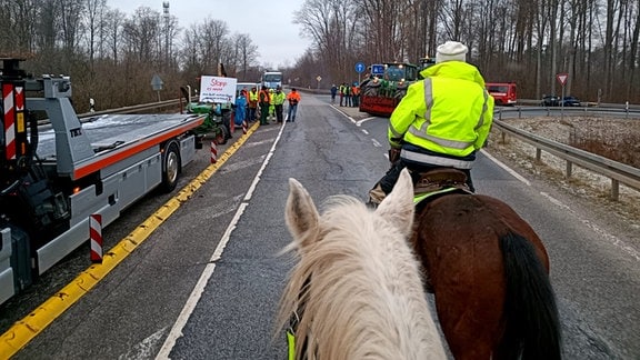 Zwei Reiterinnen nähern sich Landwirten, die mit ihren Fahrzeugen eine Kreuzung blockieren.