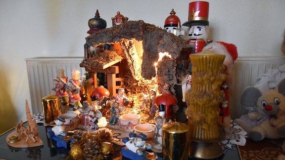 Ein Beistelltisch mit einer beleuchteten Weihnachtskrippe, Kerzen und Weihnachtsfiguren.
