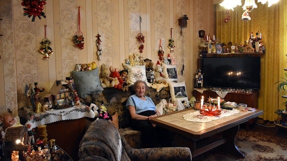 Hermine Nestler sitzt auf einem Plüschsofa inmitten von Weihnachtsfiguren.
