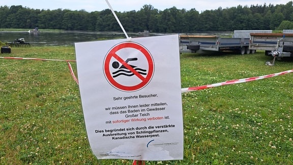 Ein Schild hängt vor einer Wasserstelle und weist darauf hin, dass man nicht im Wasser schwimmen oder baden soll.