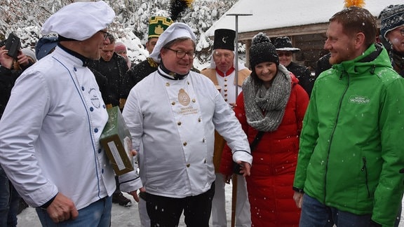 Ministerpräsident Kretschmer mit Bäckern in weißer Kleidung im Schneegestöber.