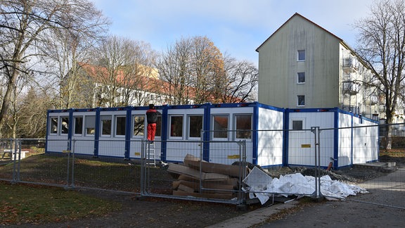 Ein Handwerker arbeitet an der Außenhülle eines Containers, der zum Schulhaus umgebaut wird.