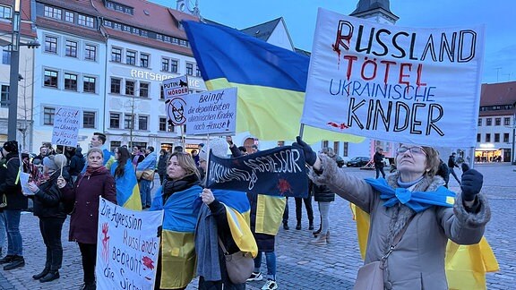 Demonstranten mit ukrainischen Flaggen halten Plakate in die Luft. 