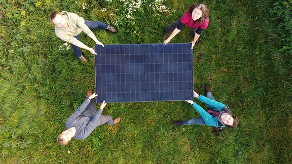 An jeder von vier Ecken eines Solarpaneels steht ein Mensch, der es festhält. Die vier Leute, jeweils zwei Frauen und zwei Männer, sind Initiatoren eines energiegenossenschafsprojektes in Mittelsachsen. 