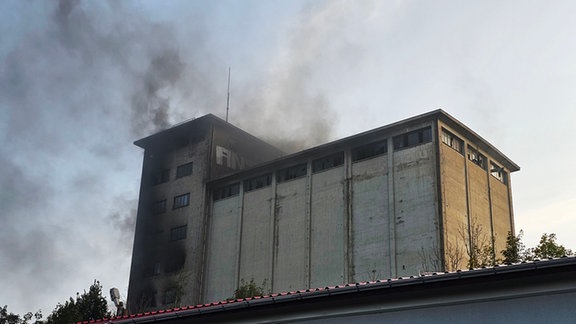 ein altes leerstehendes Silo brennt. Schwarze Schwaden steigen durchs Dach empor in den abendhimmel am 23.8.2024 in Mittweida.