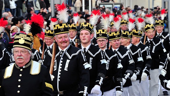 Menschen in traditioneller Bergbauuniform marschieren bei einer Parade.