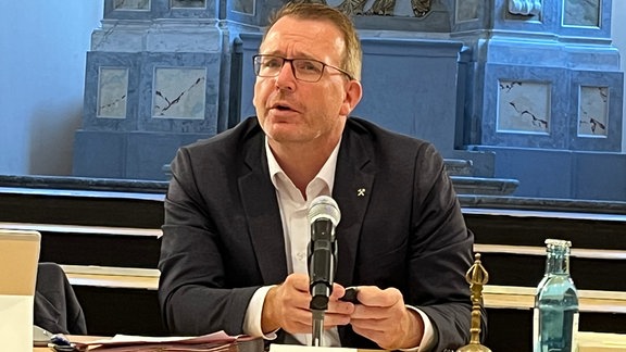 Ein Mann sitzt an einem Podium, blickt auf seine armbanduhr und wartet. Es ist der Oberbürgermeister der Stadt Freiberg, Sven Krüger.