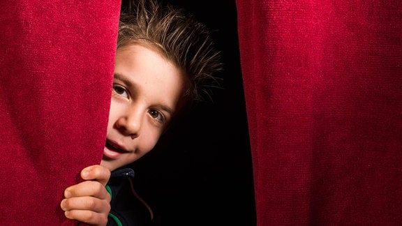 Ein Junge hinter einem roten Vorhang