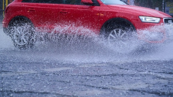 Ein Auto fährt über eine Straße, Wasser spritzt von den Reifen hoch.