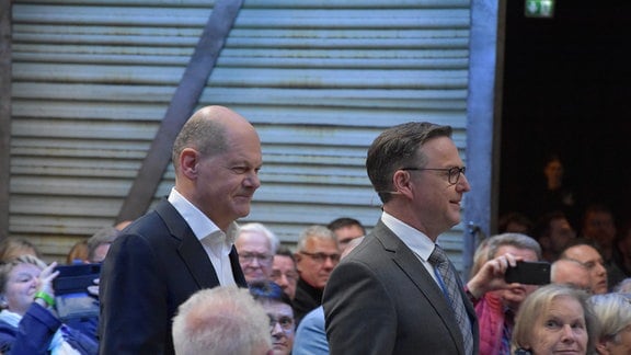 Bundekanzler Olaf Scholz und der Chefredakteur der Freien Presse, Torsten Kleditzsch laufen zwischen Zuschauern in Richtung Bühne.