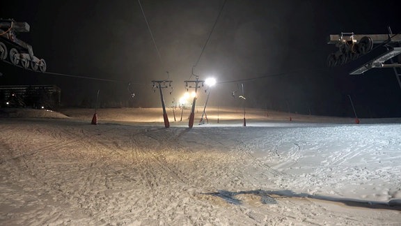 Ein menschenleerer, hell erleuchteter Skihang mit Schlepplicht bei Nacht.