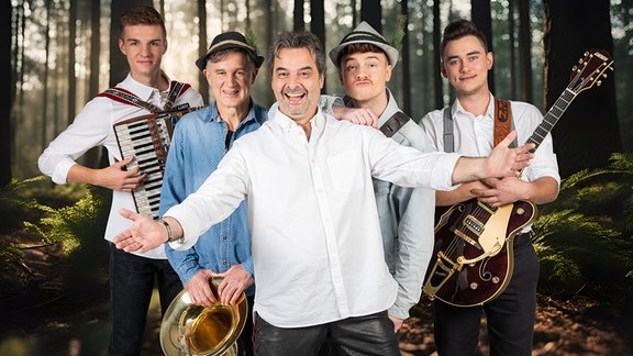 Fünf Musiker einer volksmusikband stehen mit ihren Instrumenten zusammen vor einem Hintergrund, der an den Erzgebirgswald erinnern soll. 