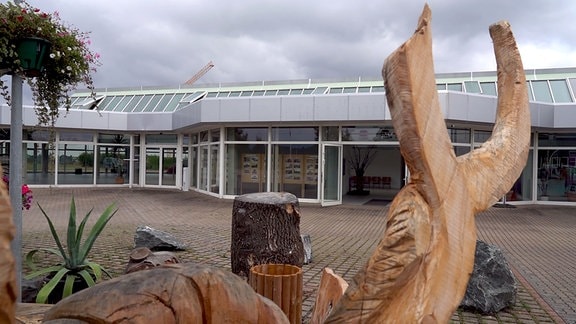 Holzskulptur vor einem eingeschossigen Gebäude