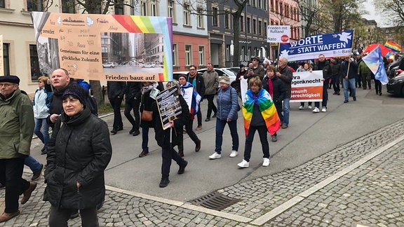Menschen laufen mit einem Transparent "Worte statt Waffen" durch eine Straße.