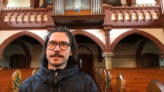 Ein junger Mann steht vor einer Orgelempore