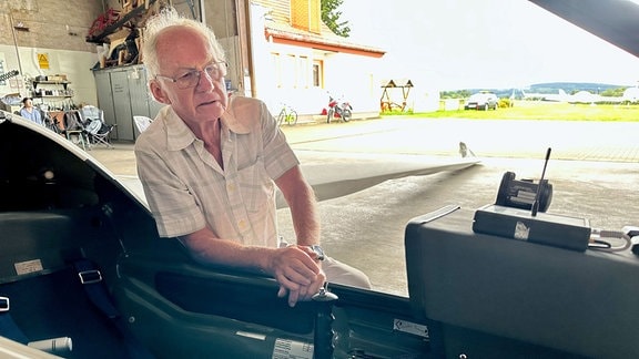 Der wahrscheinlich älteste Fluglehrer Sachsens lehnt am Cockpit eines Segelfliegers.