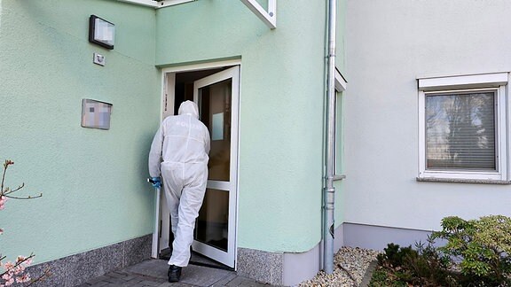 ein Mann in einem weißen Schutzanzug geht in ein modernes Mehrfamilienhaus. Es sit ein Ermittler der Spurensicherung der Polizei Chemnitz am 11.3.2024.