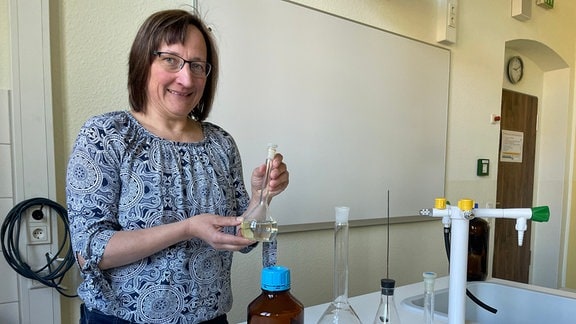 Die Chemniie- und Mathematiklehrerin Jana Bioly steht in einem Chemielabor mit einem Reagenzkolben in der Hand.