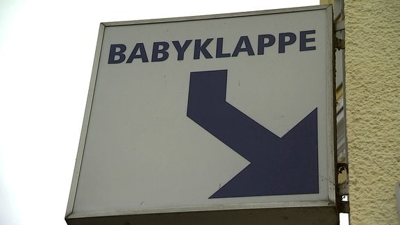 Ein Schild an einer Hauswand mit einem Pfeil und der Aufschrift "Babyklappe"