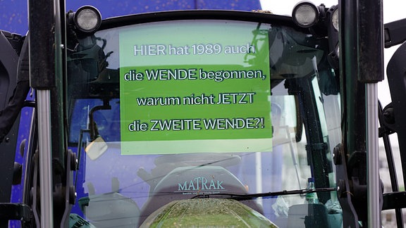 Ein Plakat mit weißer Schrift auf grünem Grund hängt an der Fensterscheibe eines Traktors. 
