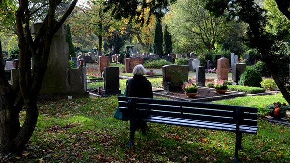 Eine Frau sitzt 2013 auf einem Friedhof auf einer Bank.