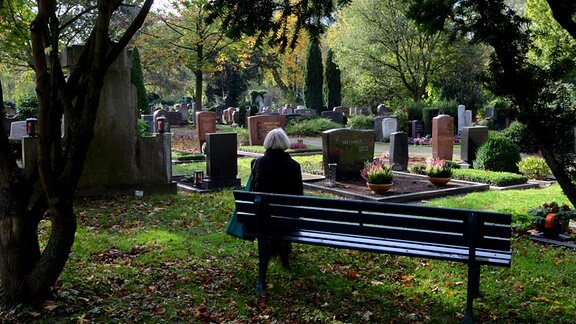 Eine Frau sitzt auf einem Friedhof auf einer Bank