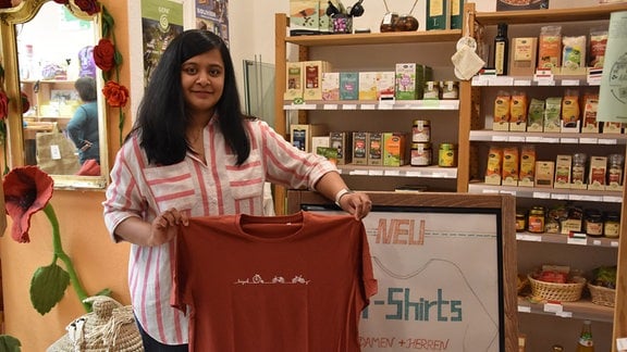 Die Inderin Nirali Patel hält ein T-Shirt negen einem selbst gestalteten Werbeaufsteller in die Kamera. 