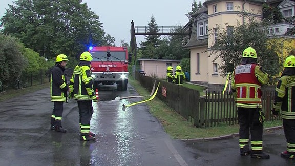 Feuerwehrmänner und ein Feuerwehrauto stehen vor einem Haus.