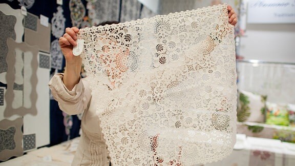 Eine Verkäuferin zeigt eine Decke vom Hersteller "Plauener Spitze".