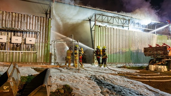 Einsatzkräfte der Feuerwehr löschen mit viel Schaum einen Scheunenbrand.