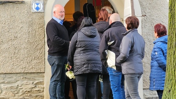 Pfarrer Tilo Kirchhoff (l) begrüßt Teilnehmer der Andacht vor der evangelischen Kirche Tirpersdorf.