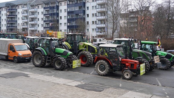 Zahlreiche Traktoren stehen nebeneinander in einer Straße vor einem Wohnblock. 