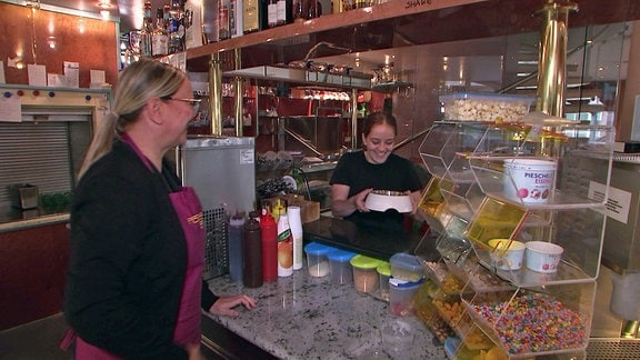 Eine Frau nimmt eine Fressschüssel für Hunde in einem Eiscafe von einer anderen Frau entgegen. 