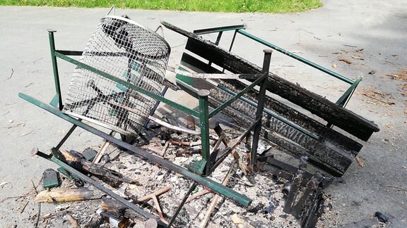 Reste von verbrannten Parkbänken liegen inmitten von Schutt und Bierflaschen.