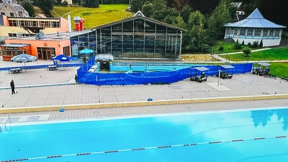 Blick auf eine Schwimmhalle hinter einem Schwimmbecken in einem Freibad.