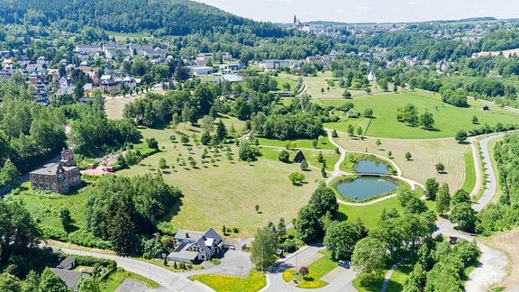 Blick von oben auf grüne Landschaft mit Wiesen, Teich, Wald und vereinzelten Häusern im Erzgebirge