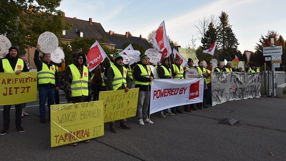 Streikende Mitarbeiter von "Paper + Design" mit gelben Westen, Verdi-Fahnen und Plakaten. 