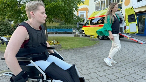 Eine Rollstuhlfahrerin im Hintergrund ein Krankentransport