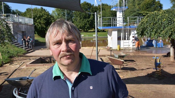 Erik Seidel, Bürgermeister von Gersdorf, steht im Freibad des Ortes vor Schubkarren und dem mit braunem Wasser gefüllten Schwimmbecken.