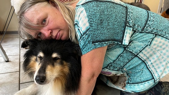 Eine Frau mit bloden Haaren umarmt ihren Hund