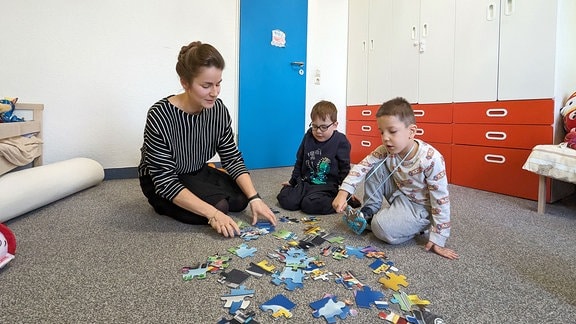 Eine Frau baut mit zwei Jungs ein Puzzle zusammen. 
