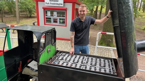 Ein junger Mann zeigt die Batterie eine Parkeisenbahn-Lok