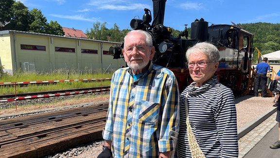 Zwei ältere Menschen stehen an einem Bahngleis.