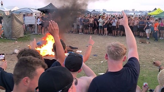 Eine große Gruppe Menschen steht johlend um ein Feuer.