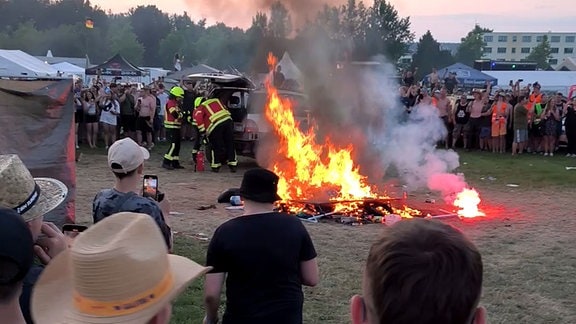 Die Feuerwehr löscht ein gelegtes Feuer. Menschen stehen darum und filmen.