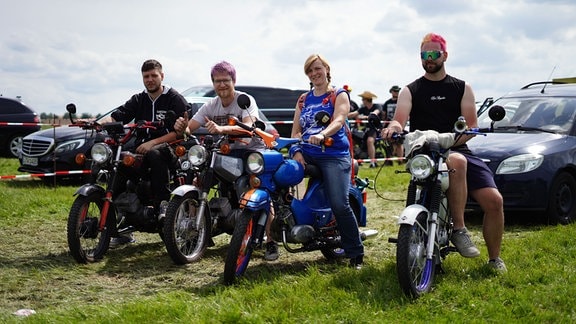 Drei junge Männer und eine Frau sitzen auf Simson Mopeds. Sie schauen freundlich in die Kamera.